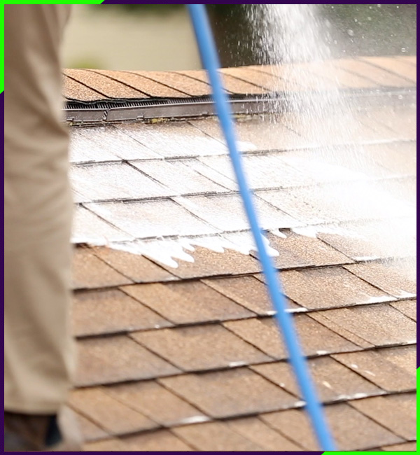 A professional worker using a pressure washer to clean a house exterior with a softwashing technique